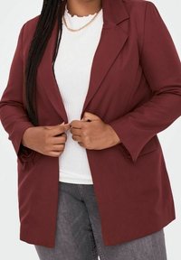 Blazer burdeos de tela suave con un diseño ajustado, que presenta solapas con muesca y un frente abierto, combinado con una blusa blanca.