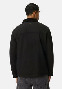 Schwarze Wollmischung-Jacke mit einem geknöpften Kragen, ausgestattet mit einer glatten Textur, nahtlosem Schulterdesign und dezentem Logodetail nahe dem Halsauschnitt.