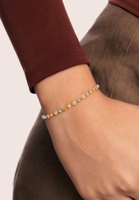 Pulsera de oro con cuentas coloridas en rosa, azul, verde y naranja. Presenta texturas suaves y eslabones delicados, llevada en una muñeca.