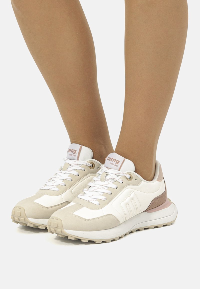Baskets avec un mélange de matériaux beige et blanc, col rembourré, design à lacets, semelle texturée et marquage subtil sur la languette.