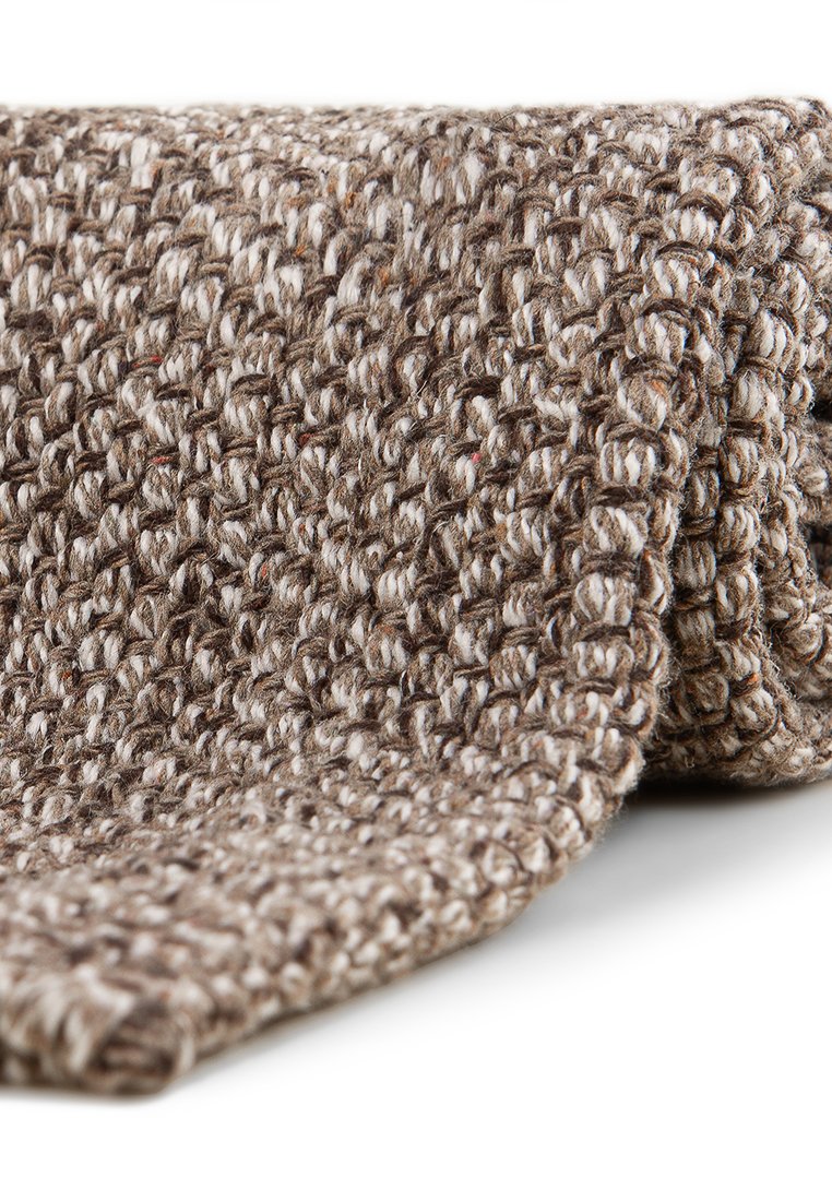 Hnědá a béžová pletenina s hrubou, texturovanou vazbou volně srolovaná na bílém povrchu.