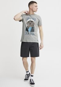 Grå bomulls t-skjorte med grafikk av en mops i en kapteinhatt, tekst "Salty Old Sea Dog." Kombinert med mørkegrå shorts og svarte joggesko.