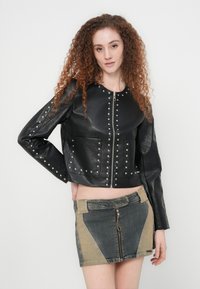 Μαύρο κοντό δερμάτινο μπουφάν με ασημένιες τρουκς, με φερμουάρ και δύο μπροστινές τσέπες, συνδυασμένο με μίνι φούστα από τζιν με αντίθετα πανελ.