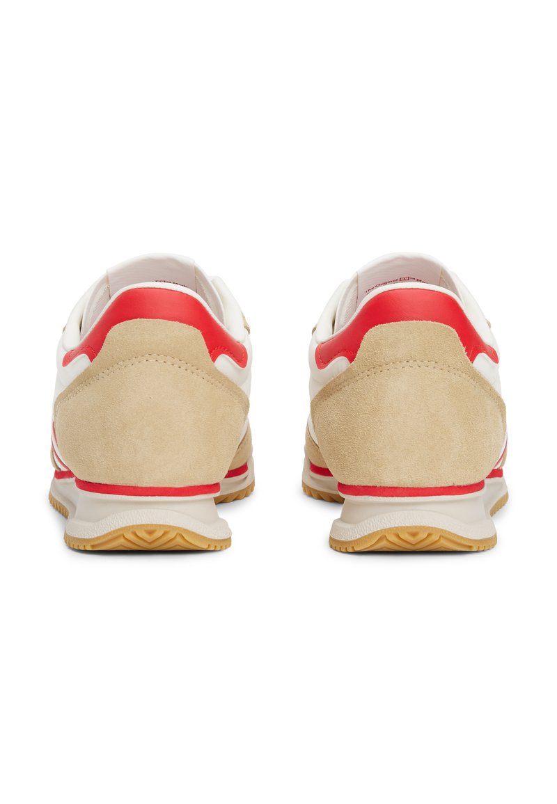 Zapatillas blancas y beige con acentos rojos, que presentan un talón de ante texturizado y una suela de goma con una banda de rodadura decorada.