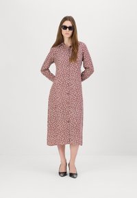 Rochie lungă cu mâneci lungi, cu flori roșii, cu închidere cu nasturi, până la jumătatea gambei și cu tocuri negre. Modelul poartă ochelari de soare închiși la culoare, stând cu mâinile la spate.