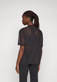 Zwarte kortemou shirt met een sheer textuur, ronde halslijn en netdetails op de mouwen. Draag het met een zwarte broek die een losse pasvorm laat zien.