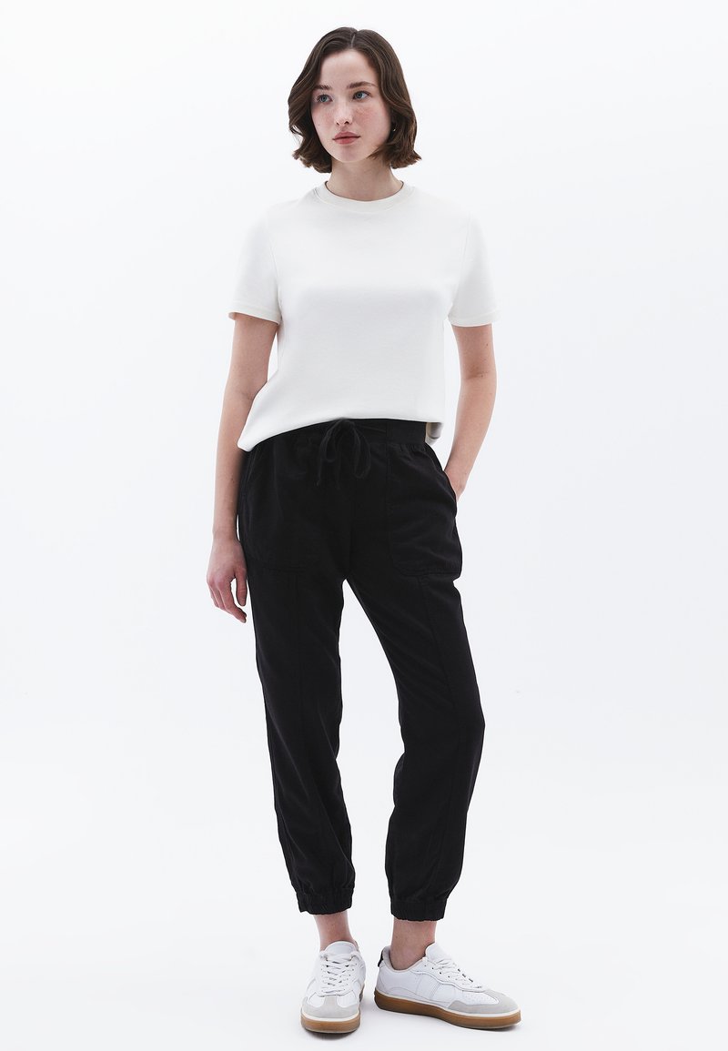 Witte shirt met korte mouwen gecombineerd met zwarte broek met trekkoord en witte sneakers. Glad materiaal en een comfortabele pasvorm; de broek heeft elastische boorden.