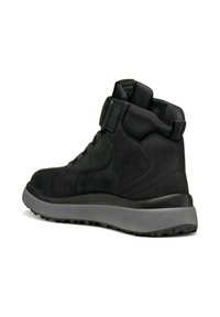 Zapatilla alta negra con parte superior de ante suave y textil, suela de goma y cierre de tira de velcro. Acentos texturizados y detalles de costura.