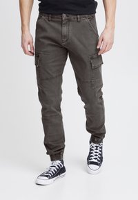 Cargo pants in dark gray fabric, featuring elastic cuffs, multiple side pockets, and a classic button closure. Worn with dark sneakers.