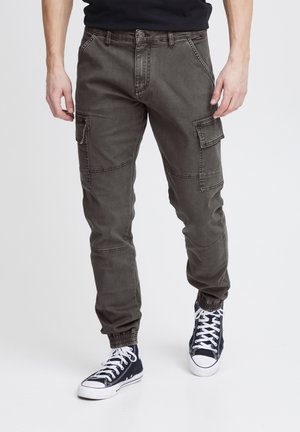 Pantalons cargo en tissu gris foncé, dotés de bords élastiques, de plusieurs poches latérales et d'une fermeture à bouton classique. Portés avec des baskets sombres.