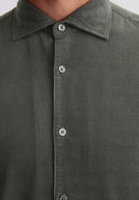 Chemise en velours côtelé vert foncé avec un col pointu et quatre boutons métalliques avec un design en étoile, mettant en valeur une texture côtelée verticale.