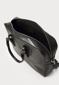 Black leather bag with a smooth finish, zippered top, two handles, and silver hardware. The interior is spacious and unlined.