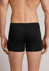 Svarta boxershorts i slät tyg, figurnära design med en bekväm midjeresår som framhäver en naturlig kontur av midja och lår.