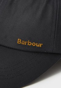 Boné preto com aba curva, apresentando "Barbour" bordado em letras amarelas pequenas no painel frontal.