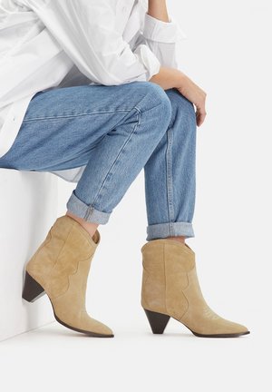 Bež antilop gležnjače sa špicastim vrhom i nazubljenim dizajnom, s smeđom blok petom i suptilnim bijelim detaljima.