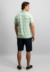 Svetle zelené pruhované polo tričko s límečkem, spárované s tmavě modrými šortkami a černými botami na slip-on. Materiál vypadá jemně a má texturu.