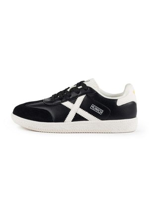 Zapatillas deportivas en blanco y negro con una parte superior de cuero texturizado, suela de goma blanca y un diseño distintivo en forma de cruz en el lateral.