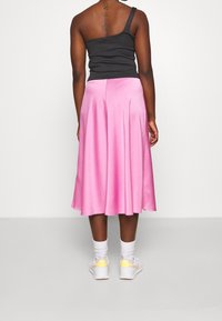 Różowa satynowa spódnica o rozkloszowanym kroju, sięgająca do połowy łydki. Noszona z czarną bluzką na jedno ramię, w połączeniu z białymi sneakerami i białymi skarpetkami.