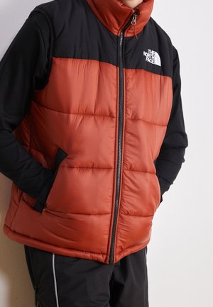 Puffy-vesti rusti-oranssissa, mustilla hartioilla, korkean kauluksen, etuvetoketjun ja sivutaskujen kanssa, valmistettu sileästä, eristetystä kankaasta.