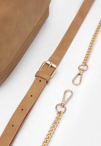 Borsa in suede beige con tracolla staccabile beige, dotata di una fibbia in metallo dorato e accenti in catena, rifinita con ganci in metallo dorato.
