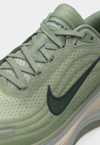 Κοντινή λήψη φωτεινού πράσινου παπουτσιού τρεξίματος Nike με κυματιστά ραφτά σχέδια, υφασμάτινο επάνω μέρος, σκούρο πράσινο λογότυπο Swoosh και παχύ, μαλακό πέλμα.