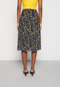 Floral pleated skirt in dark fabric with yellow, blue, and white patterns. Mid-length design with subtle texture and black heeled shoes.