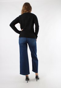 Maglione nero a maglia con silhouette aderente, abbinato a jeans in denim scuro a gamba larga. Scarpe nere con tacco alto, dettagli di cucitura discreti sui pantaloni.