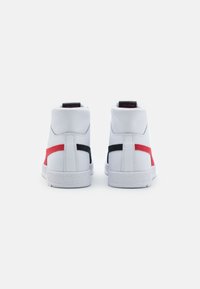 Vita högskor med röda och svarta detaljer, texturerad gummisula, slät läderöverdel och vadderad krage för stöd.