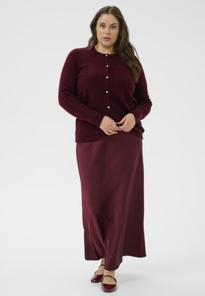Cardigan bordeaux avec fermeture à boutons, associé à une longue jupe en satin bordeaux et des ballerines fermées ; texture douce et design cintré.