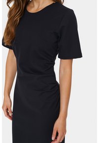 Robe noire cintrée à manches courtes, col rond, détails de fronces sur les côtés et texture lisse. Pas de fermetures ni de motifs visibles.