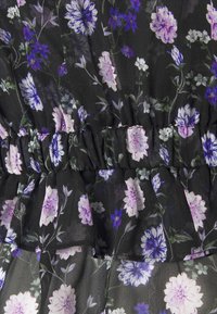 Abito nero a fiori con fiori viola e rosa, dettagli arricciati e vita elastica. Realizzato in tessuto leggero e traslucido.