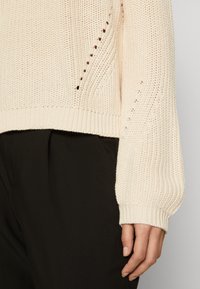 Strikket cremelilla sweater med løs pasform, ribbet manchetter og åben vævemønster. Sammen med sorte, skræddersyede bukser.