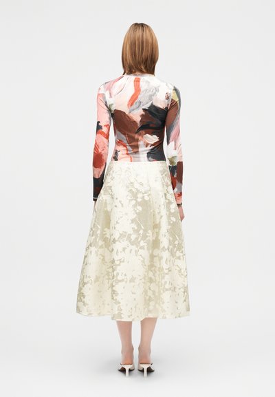 Gėlėtas ilgomis rankovėmis viršus rožinių ir rudų atspalvių, derinamas su smėlio spalvos, kulkšnies ilgio sijonu, kuriame yra tekstūruotas gėlių raštas.