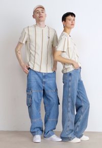 T-shirts beige à rayures associés à des pantalons cargo en denim bleu à jambes larges ; les modèles portent des baskets blanches ; tissu en coton ; coupe décontractée.