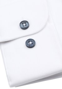 Weißes Hemd mit einem Manschettenknopf, der zwei dunkle, runde Knöpfe aufweist, die mit weißen Fäden in einem diagonalen Muster angenäht sind.