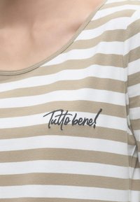 Chemise à rayures horizontales beige et blanche avec encolure dégagée, ornée d'un texte en script noir « Tutto bene ! » sur la poitrine.