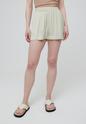 Lichtgroene shorts met een elastische tailleband, zachte textuur en een relaxte pasvorm. Gecombineerd met lichte teenslippers met een zwarte zool.