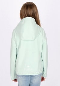 Giacca verde menta chiaro con cappuccio, texture liscia, orlo elasticizzato e logo ricamato sul retro, indossata sopra jeans blu.