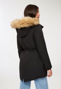 Czarna parka z kapturem wykończonym sztucznym futrem, z wąską talią i długimi rękawami, o prostym kroju i bocznych rozcięciach na końcu.