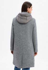 Cappotto in lana grigia con finitura testurizzata, dotato di cappuccio grigio imbottito e staccabile. Maniche lunghe e design a taglio dritto.