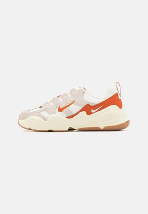 Biało-beżowy sneaker z pomarańczowymi akcentami, falistą podeszwą, cholewką z siateczki i zamszu oraz logo Nike swoosh po bokach i na pięcie.