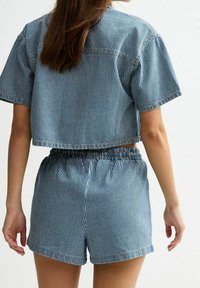 Top croppato in denim a righe con maniche corte e pantaloni a vita elastica abbinati. Rigature verticali blu e bianche, vestibilità casual, cuciture visibili.