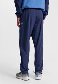 Mörkblå träningsbyxor med elastisk midja och mudd, med sidofickor och en diskret logotyp på vänster bakficka.