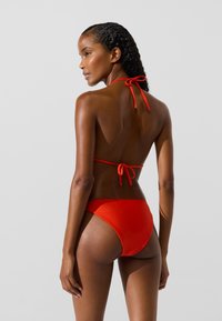 Raudonas bikini komplektas su nuimama kaklo juosta ir klasikiniu apatine dalimi. Lygus, vienspalvis audinys. Minimalistinis dizainas su patogiu pritaikymu.