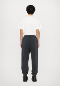 Schwarze Sweatpants mit elastischen Abschlüssen, im entspannten Schnitt und mit Logo-Druck an der Seite, kombiniert mit einem schlichten weißen T-Shirt.