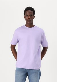 Camiseta de manga corta y cuello redondo en tela de algodón de color púrpura claro, con un corte holgado y sin patrones ni adornos visibles.