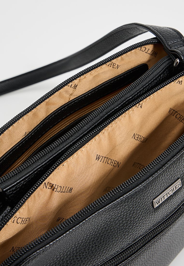 Schwarze Lederhandtasche mit strukturierter Oberfläche, ausgestattet mit mehreren Reißverschlussfächern und einem beigen Innenfutter, das mit "Wittchen" gekennzeichnet ist.