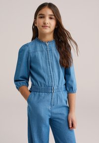 Világoskék farmer overál. Zipzáras elülső, rövid, puffos ujjú, elasztikus derékpánttal és oldalsó zsebekkel. Puha, hétköznapi anyag.