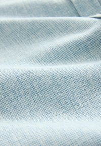 Tissu bleu clair avec un motif tissé texturé et des plis doux créant des ombres et des reflets subtils.