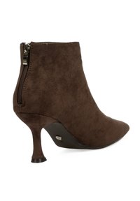 Botín de ante marrón con puntera puntiaguda y tacón delgado. Cuenta con una cremallera lateral y una textura suave con detalles mínimos.